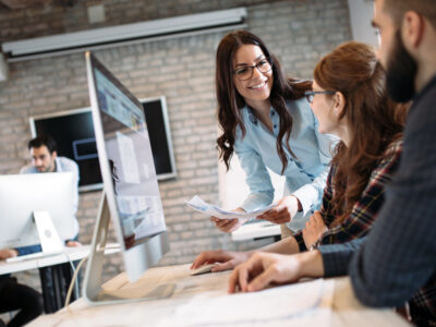 female office worker leans in with a helpful smile at desk