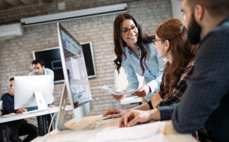 female office worker leans in with a helpful smile at desk